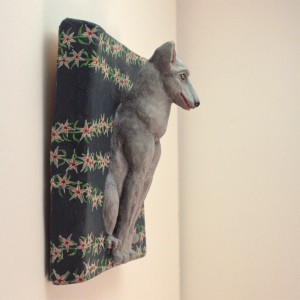 sitzender Wolf auf dunkelblaugrauem Untergrund auf dem sich sternförmige Blüten ranken. Seitliche Ansicht von halbrechts.