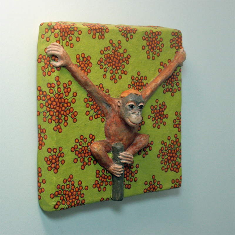 Ein rot-brauner Orang-Utan hockt auf einer Stange und hält sich mit ausgebreiteten Armen am Bildrand fest. Der Hintergrund ist hell olivgrün, darauf kleine kugelige Gebilde in rot. Ansicht halb seitlich.